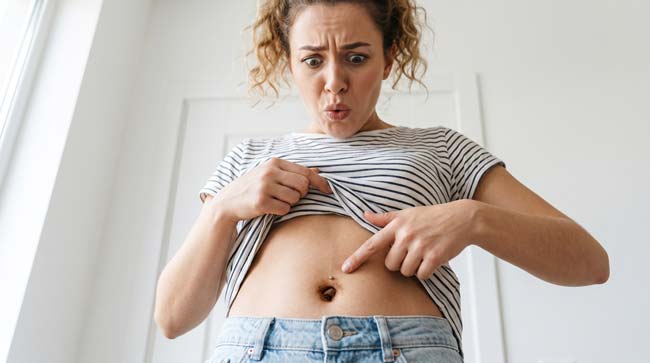A person looking surprised at their dirty neglected belly button illustrating what happens when the navel is never cleaned including bacterial buildup dead skin accumulation sebum deposits and potential omphalolith formation
