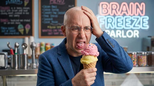 A man holding an ice cream cone wincing in pain and grabbing his forehead experiencing brain freeze illustrating how cold food triggers sphenopalatine ganglion activation and trigeminal nerve pain