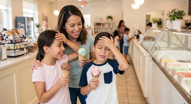 Woman and children pressing tongue to the roof of mouth to stop brain freeze pain while holding an ice cream cone illustrating the fastest science-backed method to relieve sphenopalatine ganglion activation