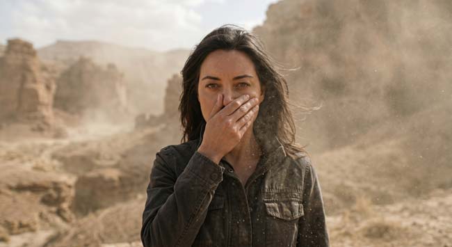 A person covering their nose and mouth in a dusty environment illustrating how the body's mucociliary escalator cough reflex and alveolar macrophages work to remove inhaled particles from the airways