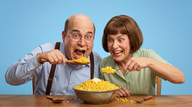 Two people enthusiastically eating corn from a large bowl illustrating the science of what happens to the human body when corn becomes the sole food source leading to vitamin B3 deficiency and pellagra symptoms