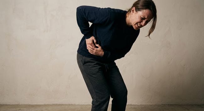 A person doubled over in severe flank pain clutching their side illustrating what happens when you pass a kidney stone including ureteral spasm hydronephrosis pressure and renal colic described as among the most intense pain the human body can experience