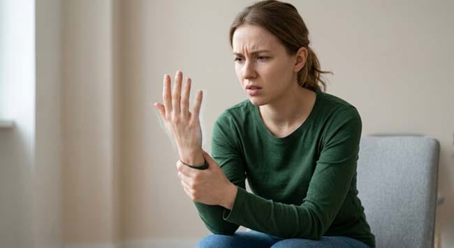 A person looking confused at their tingling hand illustrating what is paresthesia the abnormal sensation of pins and needles produced by spontaneous nerve firing without external stimulus from causes ranging from positional compression to serious neurological conditions