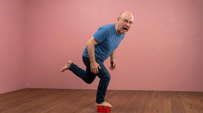 A person hopping in extreme pain after stepping on a LEGO brick illustrating why stepping on a LEGO hurts so much from pressure concentration physics foot nerve density and rapid nociceptor cascade activation